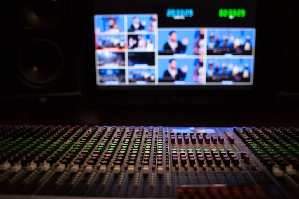 Services Close-up of a sound mixer with screens displaying video feeds in a professional studio setup.